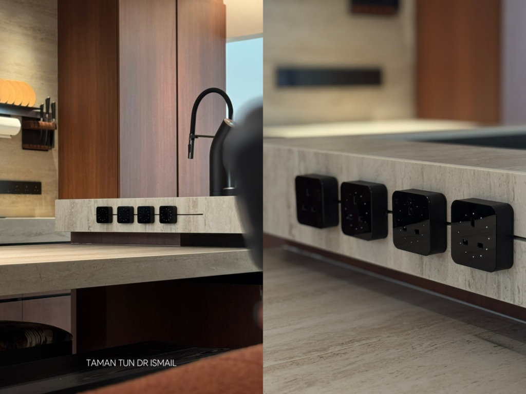 Close-up of a kitchen island with a thick sintered stone countertop featuring a built-in row of black power sockets and switches, shown in a modern Taman Tun Dr Ismail home.